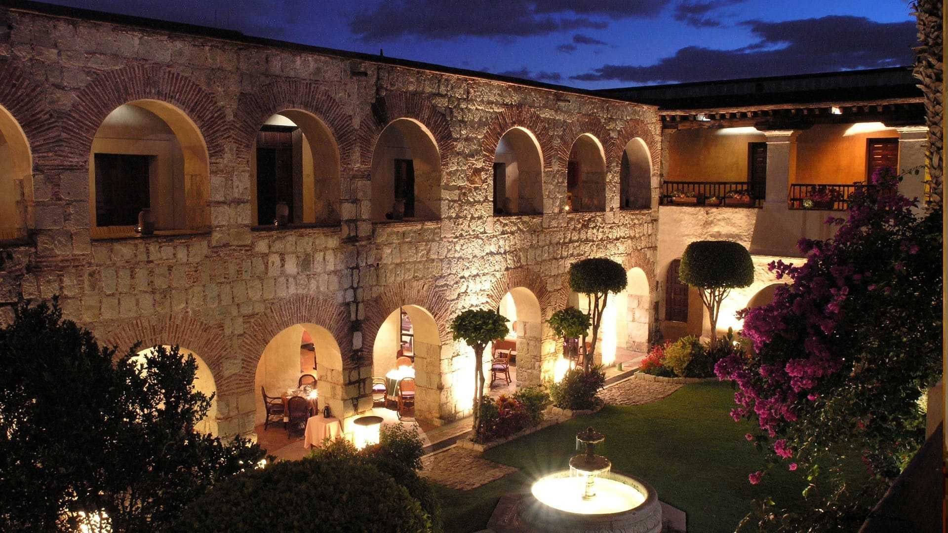 Historic stone courtyard with arches and a fountain at night near Quinta Real Oaxaca hotel