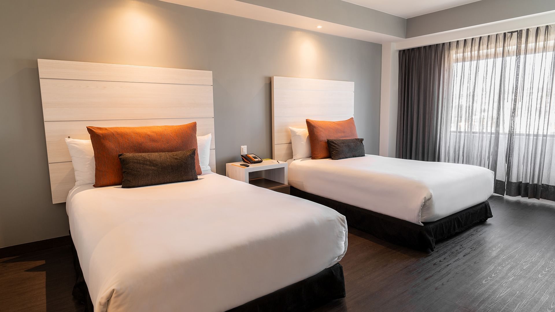 Two Double Master Suite featuring cozy beds with orange pillows and warm overhead lighting at Real Inn Tijuana