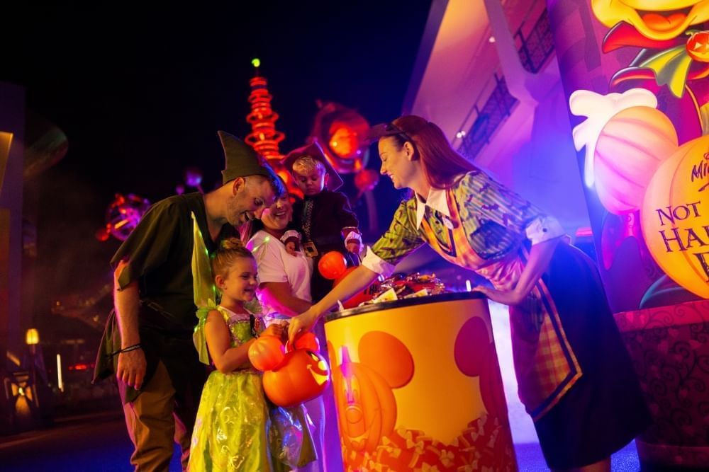 A family in Peter Pan themed costumes receive candy from a Disney cast member at night.