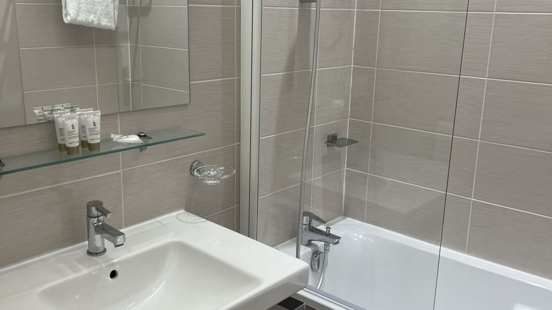 Bathroom with white sink, mirror, shower, and bathtub with towels and toiletries.