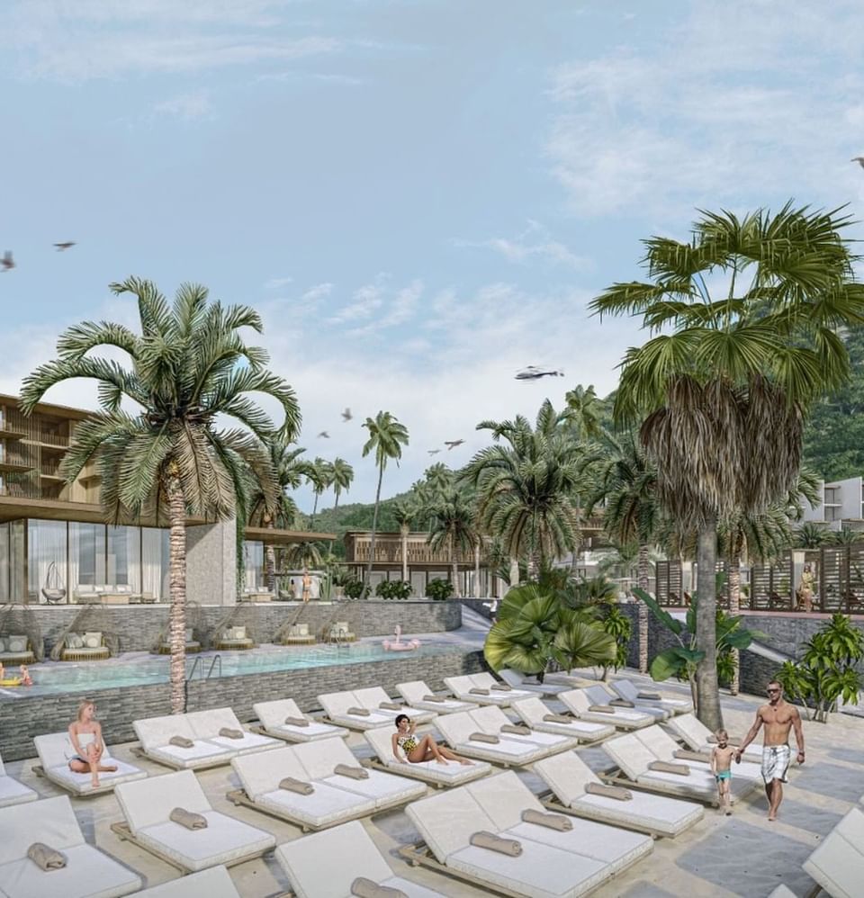 Tropical pool and beach lounge area at A'ila Resorts, with sunbeds and palm trees under a sunny sky
