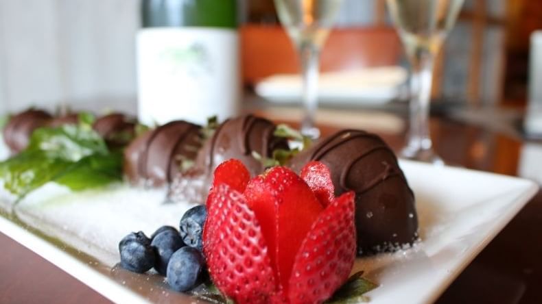 Chocolate-covered strawberries, blueberry, rose strawberry, and wine glasses on a plate for Romance Package.