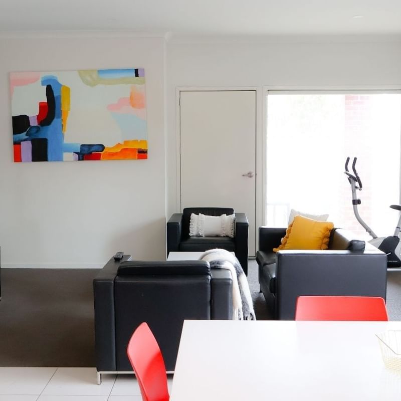 Modern living room with black furniture, a bright painting, and a balcony at La Trobe University Regional Housing.
