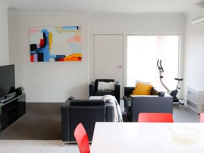 Modern living room with black furniture, a bright painting, and a balcony at La Trobe University Regional Housing.