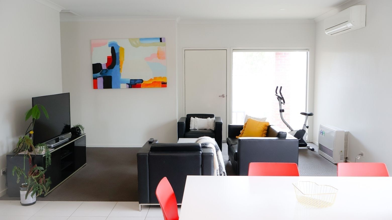 Modern living room with black furniture, a bright painting, and a balcony at La Trobe University Regional Housing.