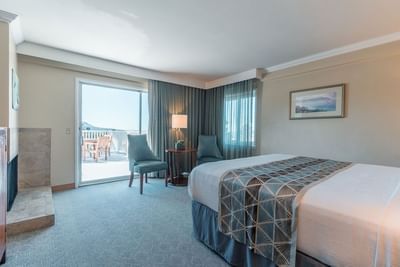 A comfortable hotel room featuring a king bed, fireplace, and sliding door to a balcony at Carmel Bay View Inn