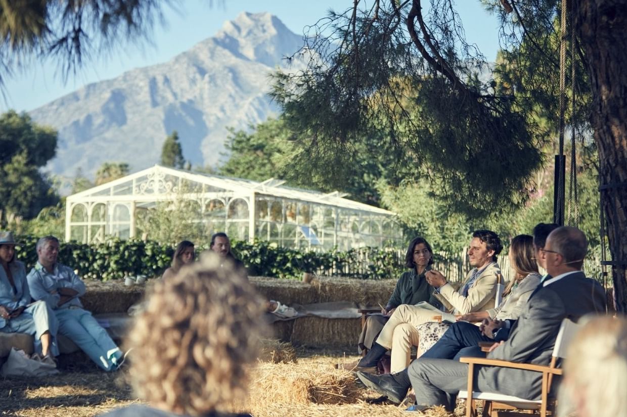 Guests gathered for an outdoor talk at Marbella Club with La Concha mountain and a white glasshouse in the backdrop