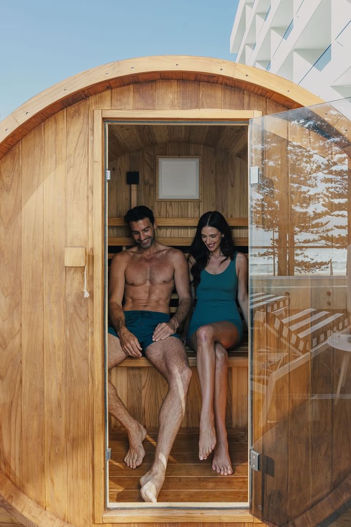 Barrel sauna at Elysium Manly featuring a smiling man and woman sitting together while looking down within the timber