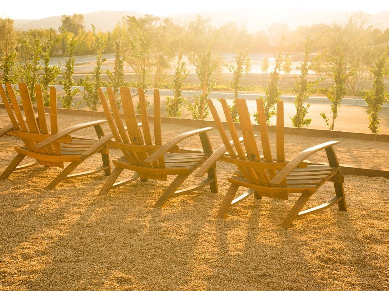 Three wooden lounge chairs facing towards sunset and vineyard