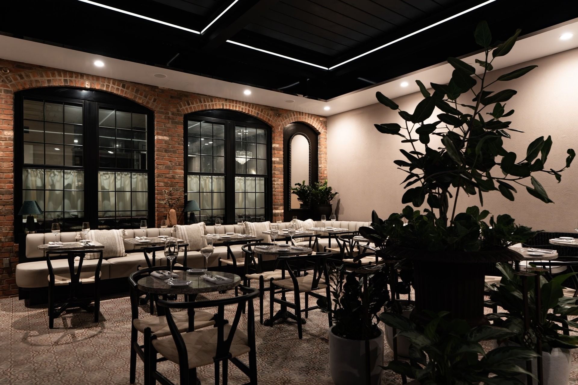 A dining area with tables and chairs, a couch, and large windows.