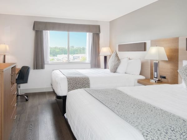 Hotel room with two queen beds, TV, chair, table, mirror, and window