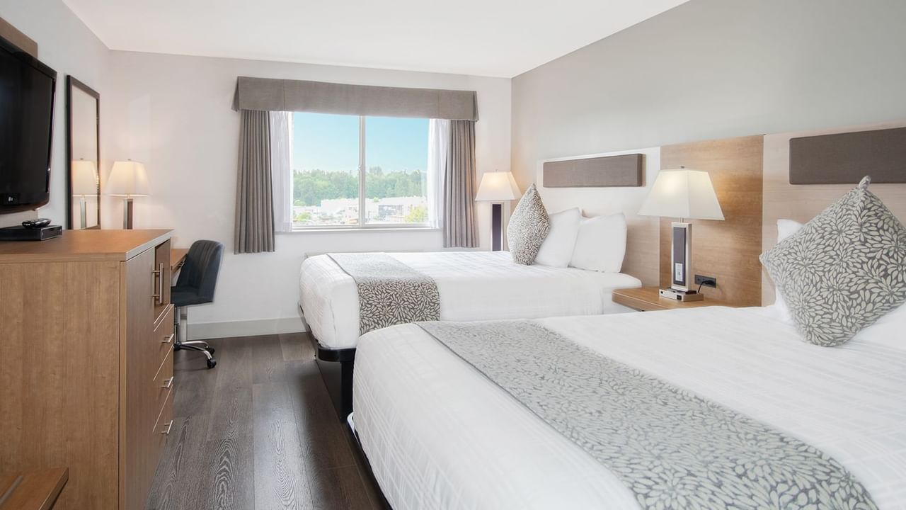 Hotel room with two queen beds, TV, chair, table, mirror, and window