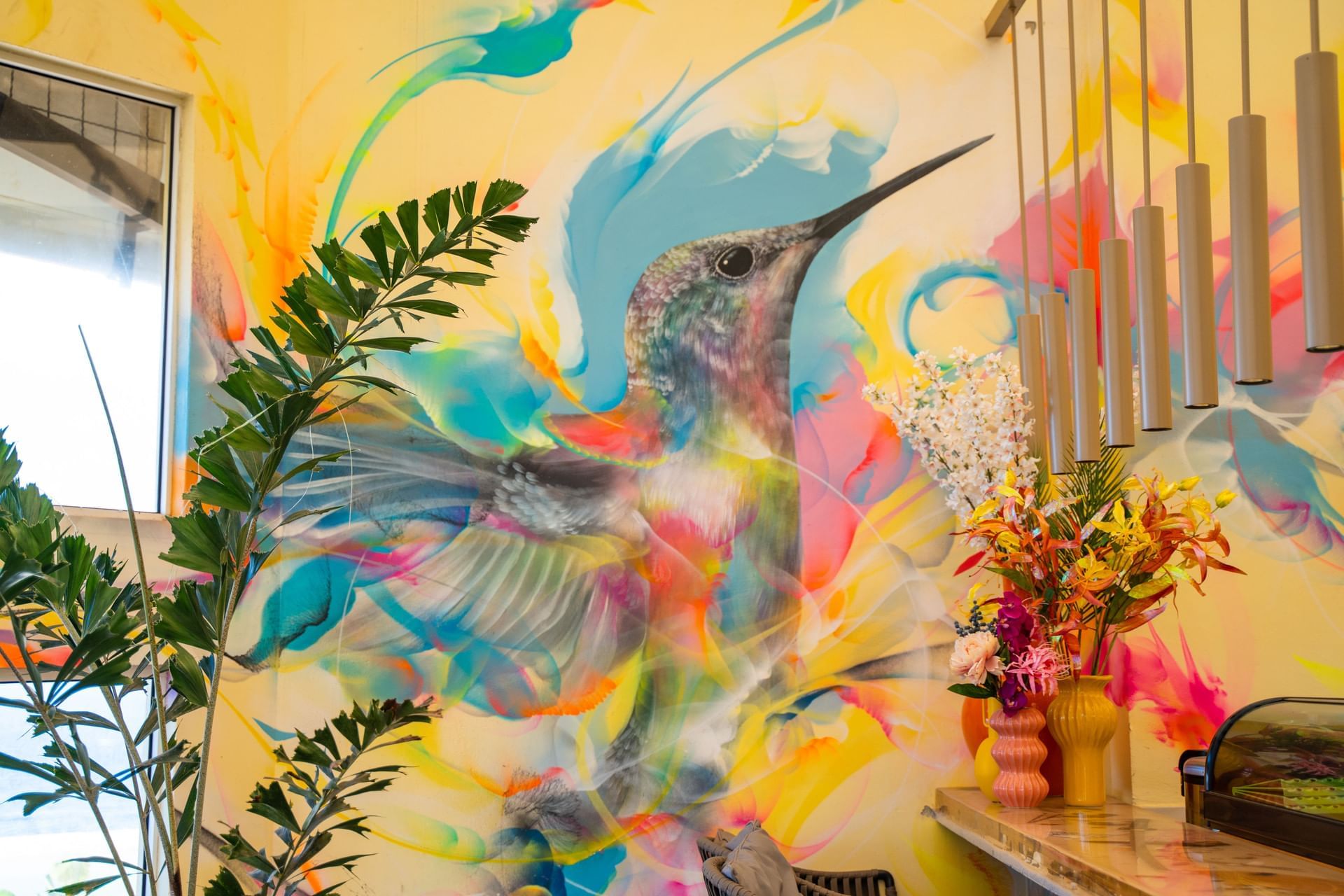 Kolibrie-muurschildering met kleurrijke spiralen, kamerplanten en bloemen in Bobbie’s Beach Club bij Golden Rock Resort