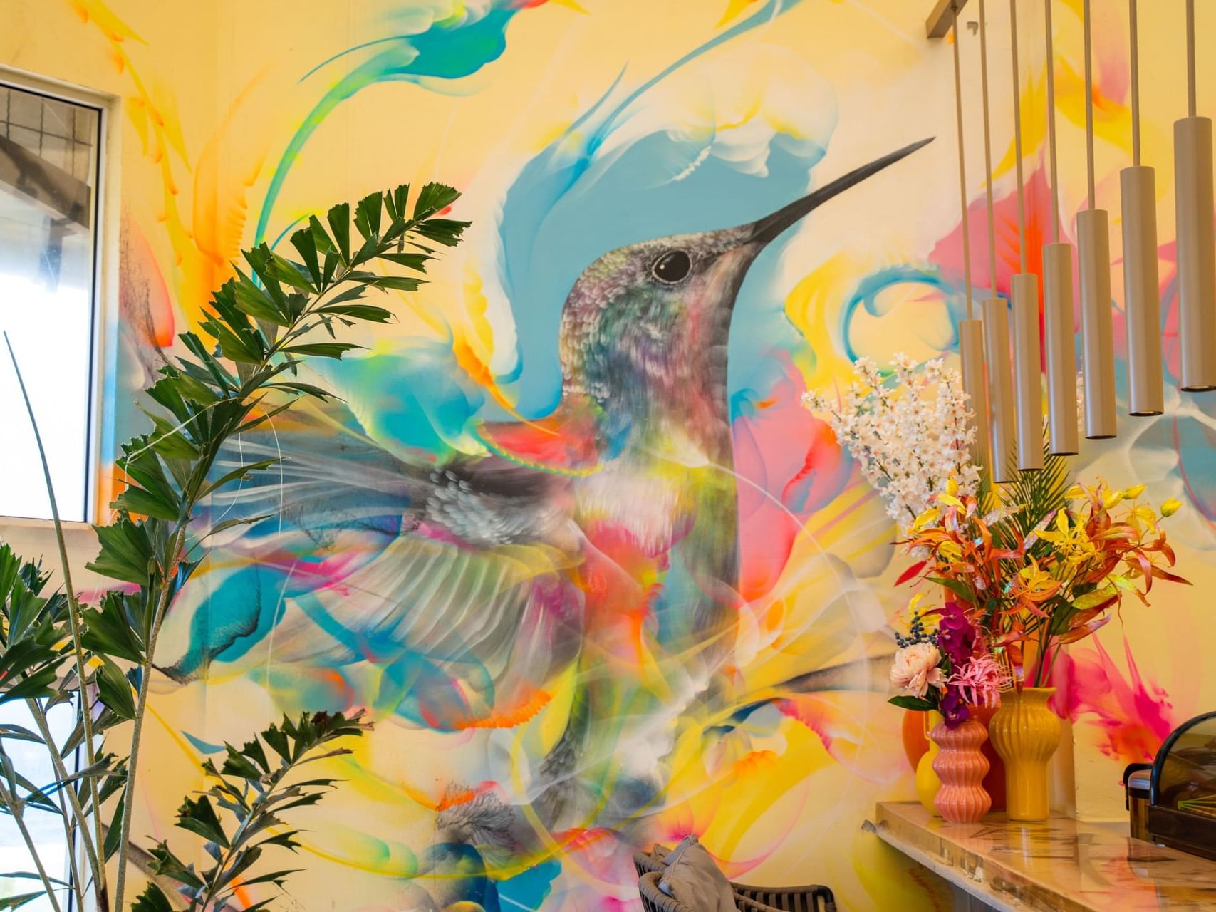 Kolibrie-muurschildering met kleurrijke spiralen, kamerplanten en bloemen in Bobbie’s Beach Club bij Golden Rock Resort