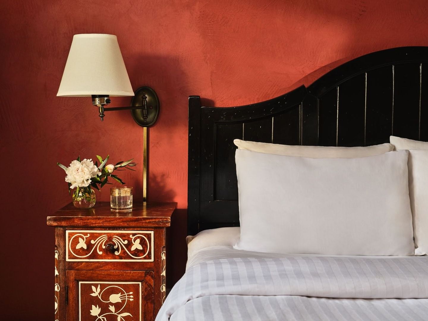 Demi Suite featuring red textured wall behind a black headboard and wooden nightstand with white lamp at Petit Ermitage