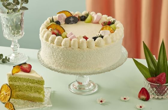 Close-up of a cake topped with fruits and candies with a slice of cake served at Hanoi Daewoo Hotel