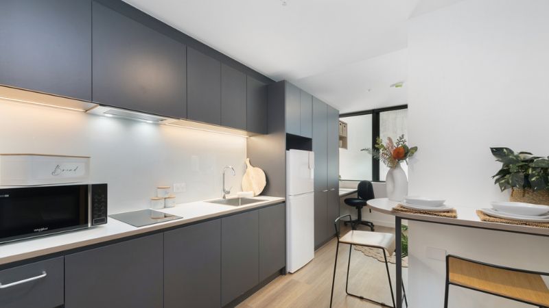 Modern kitchen with gray cabinets, white appliances, wooden floors, and a dining area with a vase of flowers.