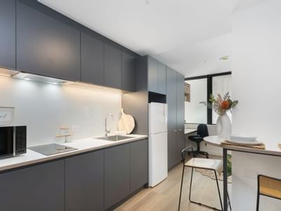 Modern kitchen with gray cabinets, white appliances, wooden floors, and a dining area with a vase of flowers.