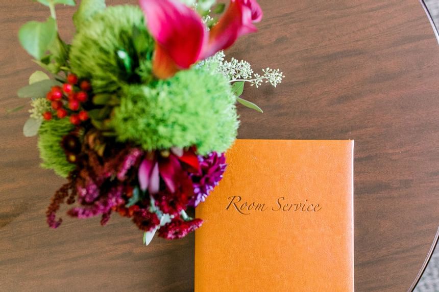 Orange room service menu booklet on a wooden table beside colorful flowers at Clemson University Conference Center & Inn