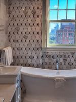 White soaking tub by a marble sink under a window with a city view in Presidential Suite at Warwick Melrose Dallas