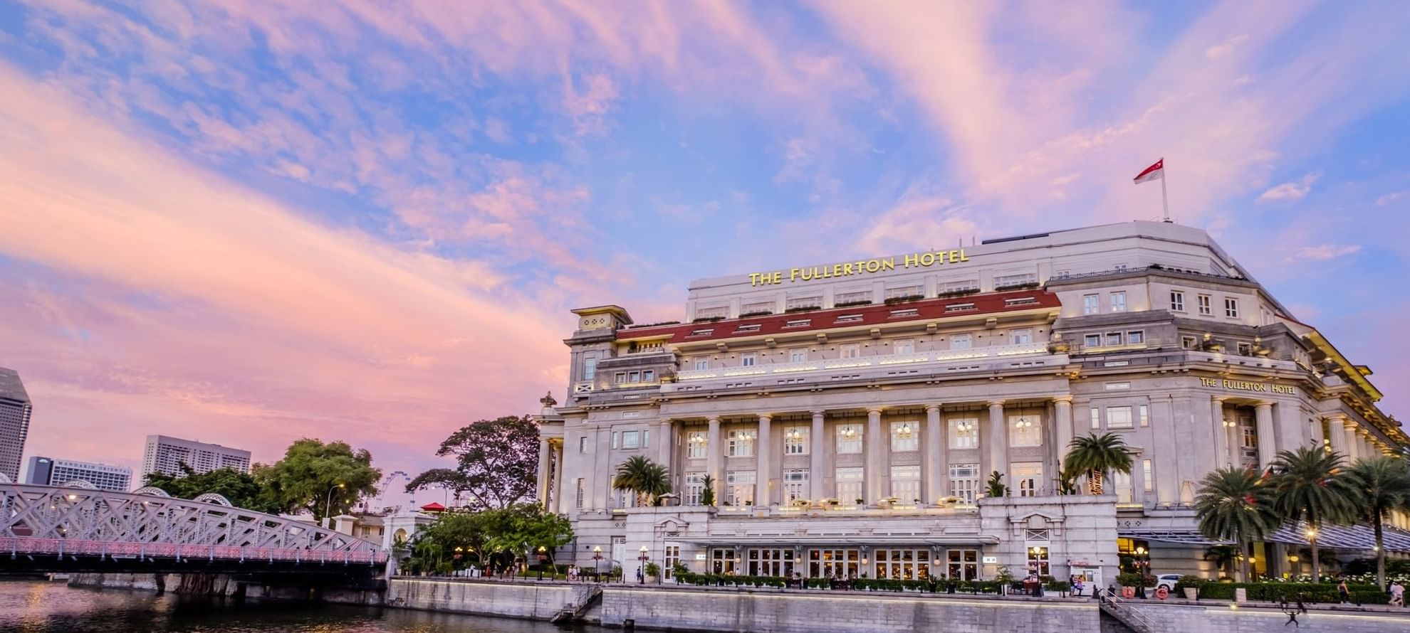 Exterior of The Fullerton Hotels and Resorts by the water at dusk with a vivid pink and blue sky