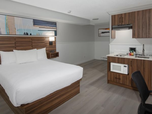 Queen-sized bed with white linens and a kitchenette with refrigerator.