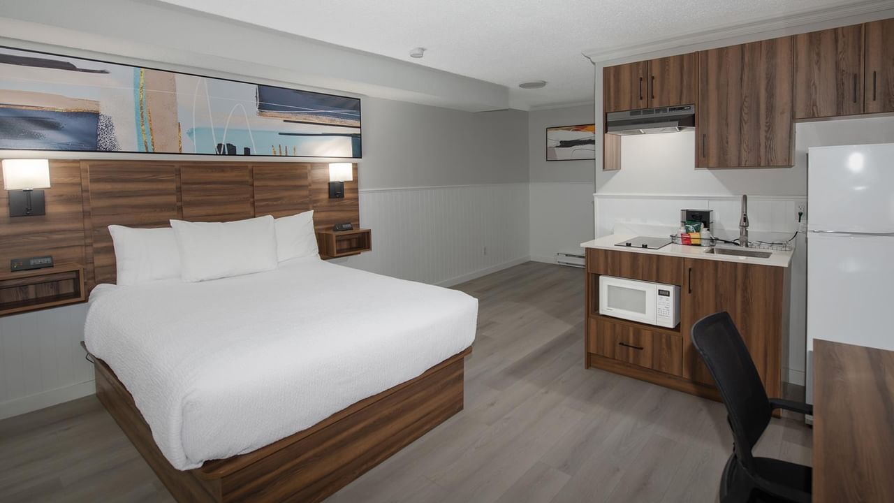 Queen-sized bed with white linens and a kitchenette with refrigerator.
