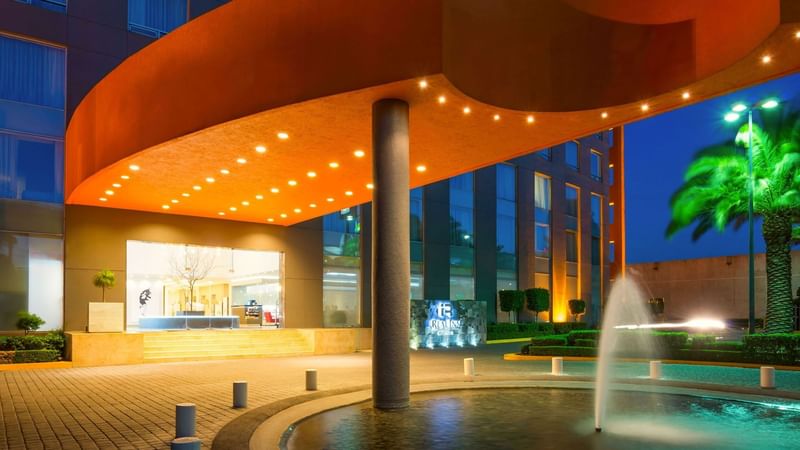 Illuminated entrance featuring a bright orange canopy, water fountain, and modern design at Real Inn Perinorte