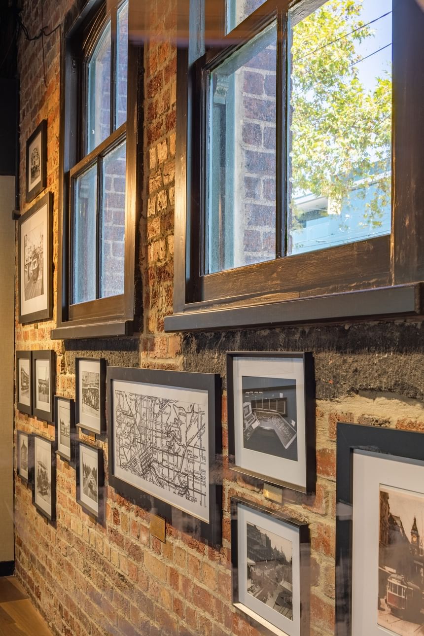 Exposed brick wall with framed black and white photographs and two windows at Amora Herencia Riverwalk Melbourne