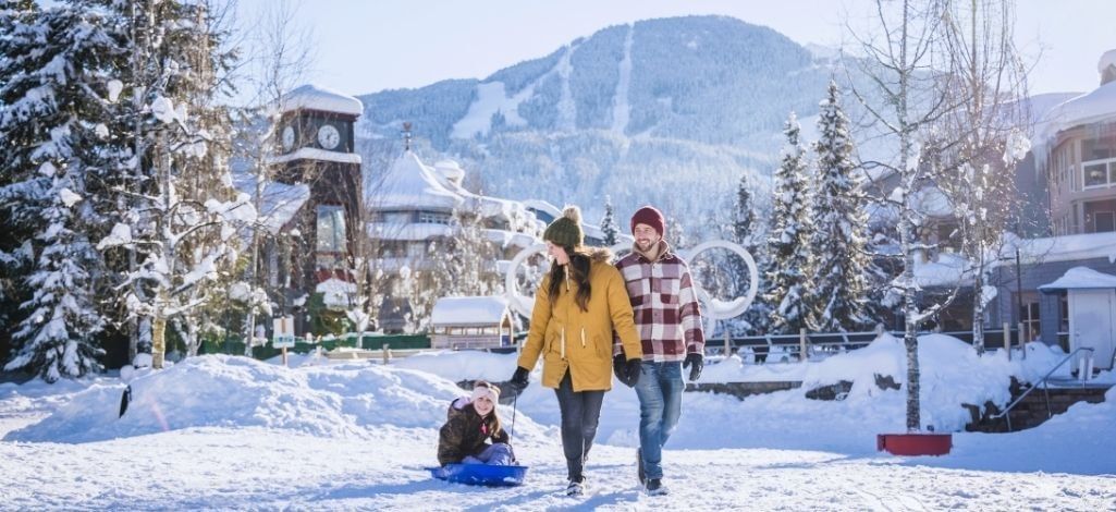 Family walking through Whistler Village in winter with a child sled