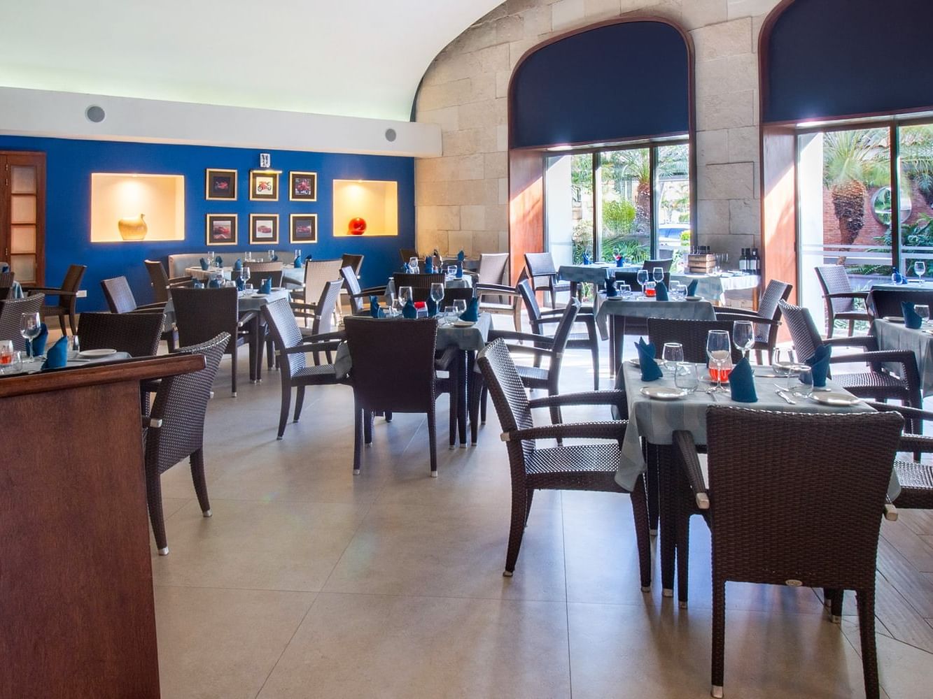 Restaurante Caruso con mesas junto a ventanas arqueadas y pared azul en Guadalajara Plaza Hoteles & Suites