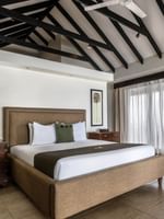 White bedding with two dark wood dressers and grey armchair in Shefa Pool Villa at warwick le lagon-vanuatu