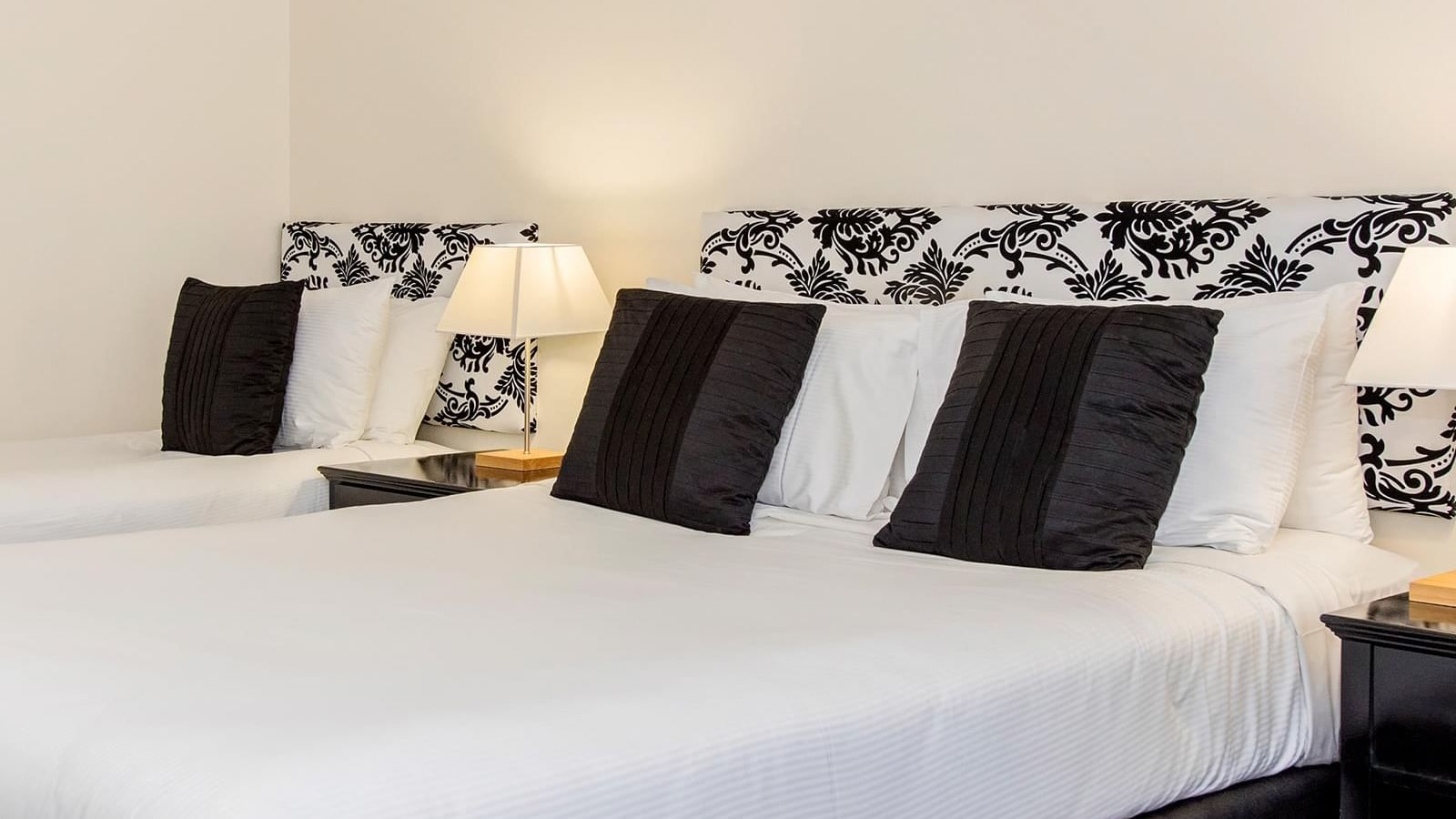 Interior of a hotel room with a black and white patterned headboard with lamps on the nightstand at Mercure Charlestown