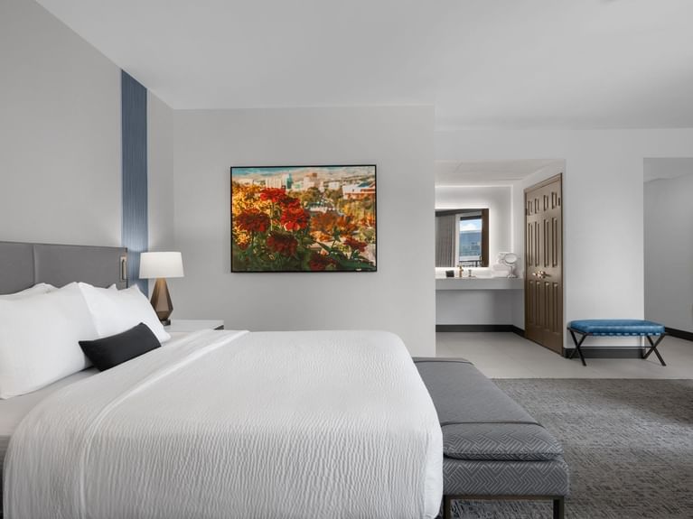 Latitude Suite with a large bed, a painting of red flowers on the wall, and a view of the bathroom vanity at Hotel 43 Boise