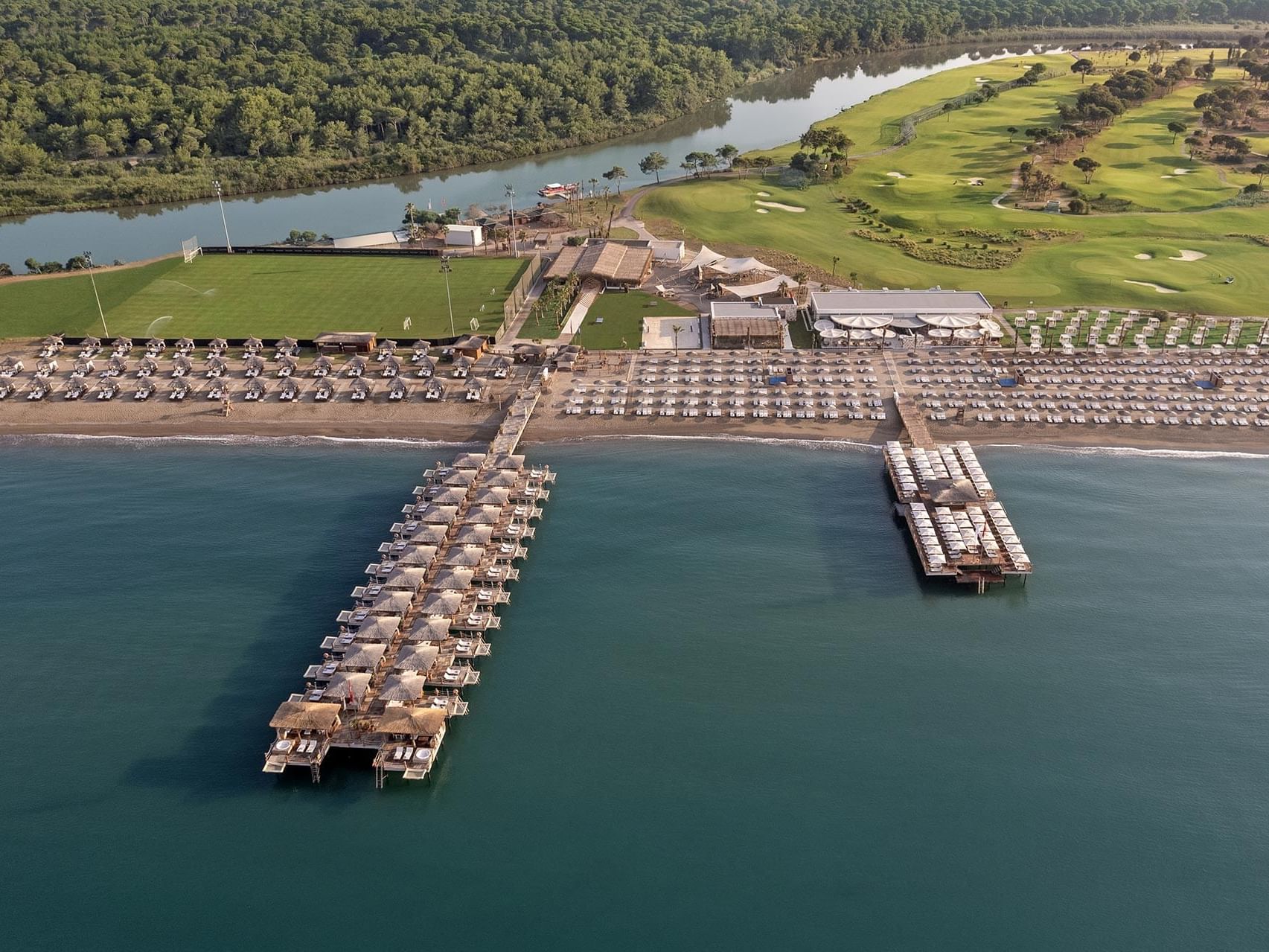 Aerial view of Titanic Deluxe Golf Belek with lined beach umbrellas, piers, and a river