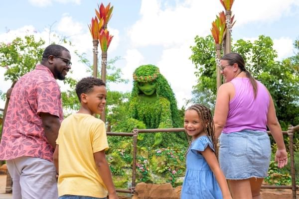 A man, woman, boy, and girl smile in front of a topiary figure of Te Fiti from Moana at EPCOT. 