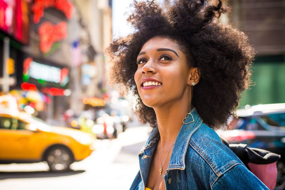 Smiling woman with a natural afro explores the sunny city streets by Warwick New York