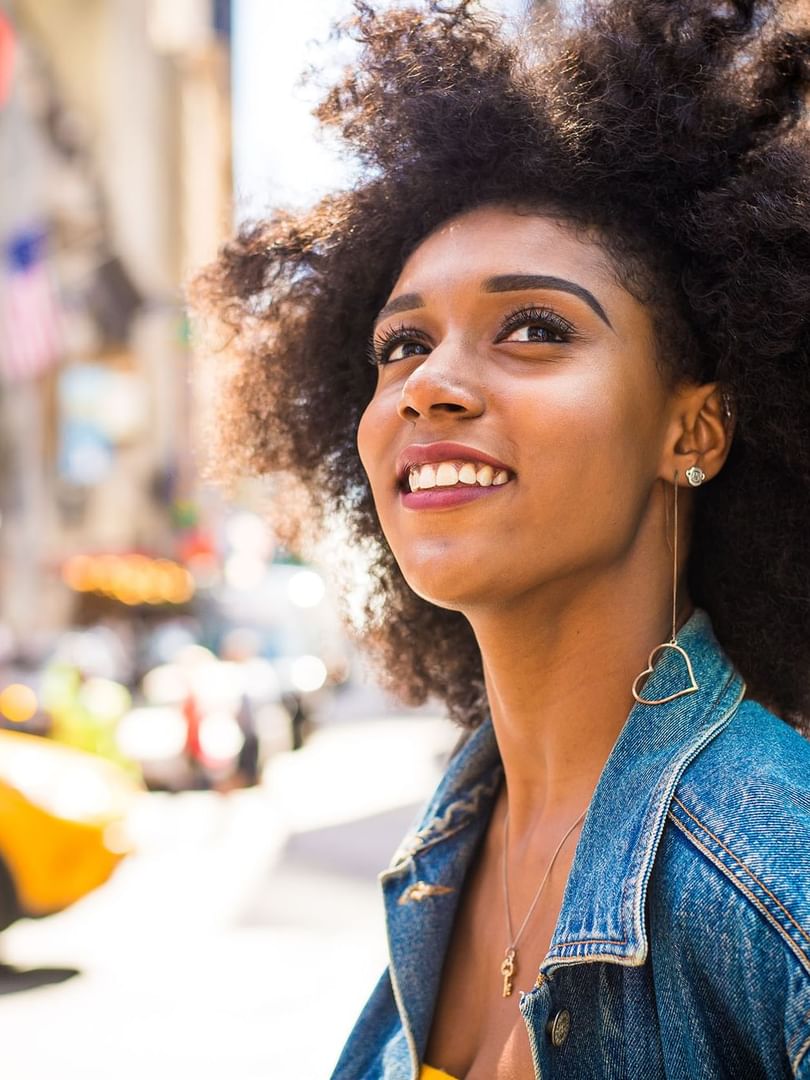 Young woman with curly hair looking upward by a bustling city street near Warwick New York