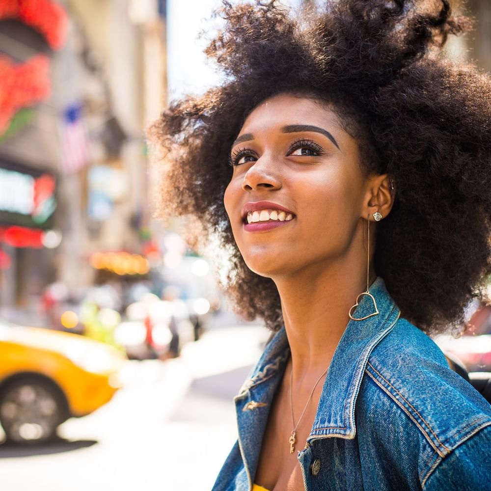 Young woman with curly hair looking upward by a bustling city street near Warwick New York