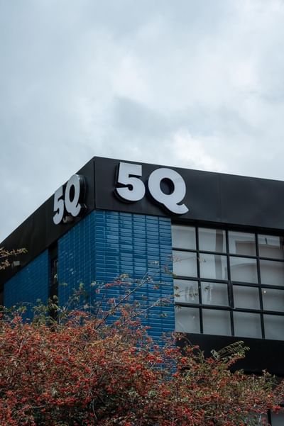 Modern corner view with bold white 5Q signage on dark panel and blue brick walls at 5Q House Zona G under cloudy sky