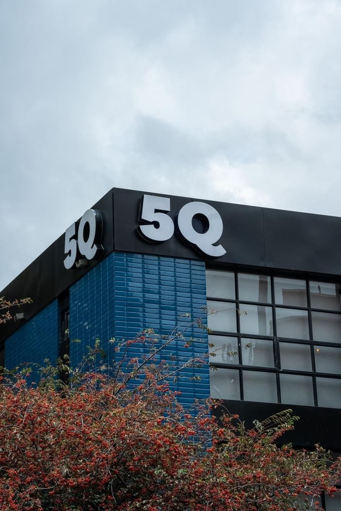 Modern corner view with bold white 5Q signage on dark panel and blue brick walls at 5Q House Zona G under cloudy sky