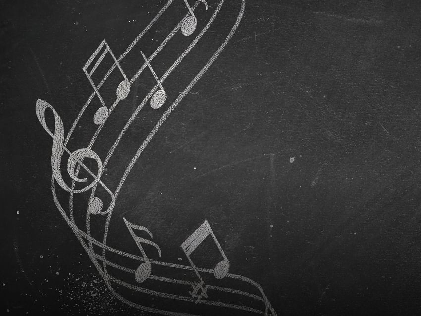White chalk musical notes and a treble clef flowing across a textured black chalkboard surface at Camino Real