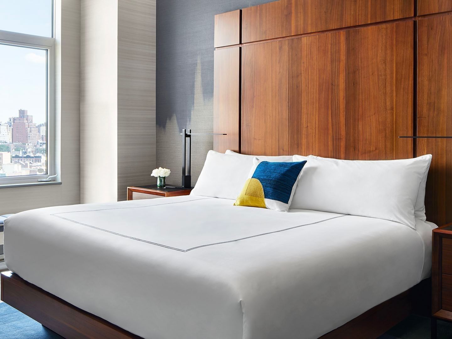 A hotel room with a large bed, wooden headboard, two nightstands, and a city view.