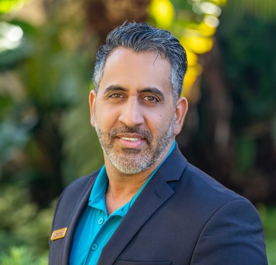 Miguel Bouret in suit jacket over teal polo shirt standing before greenery at Rosen Inn at Pointe Orlando garden