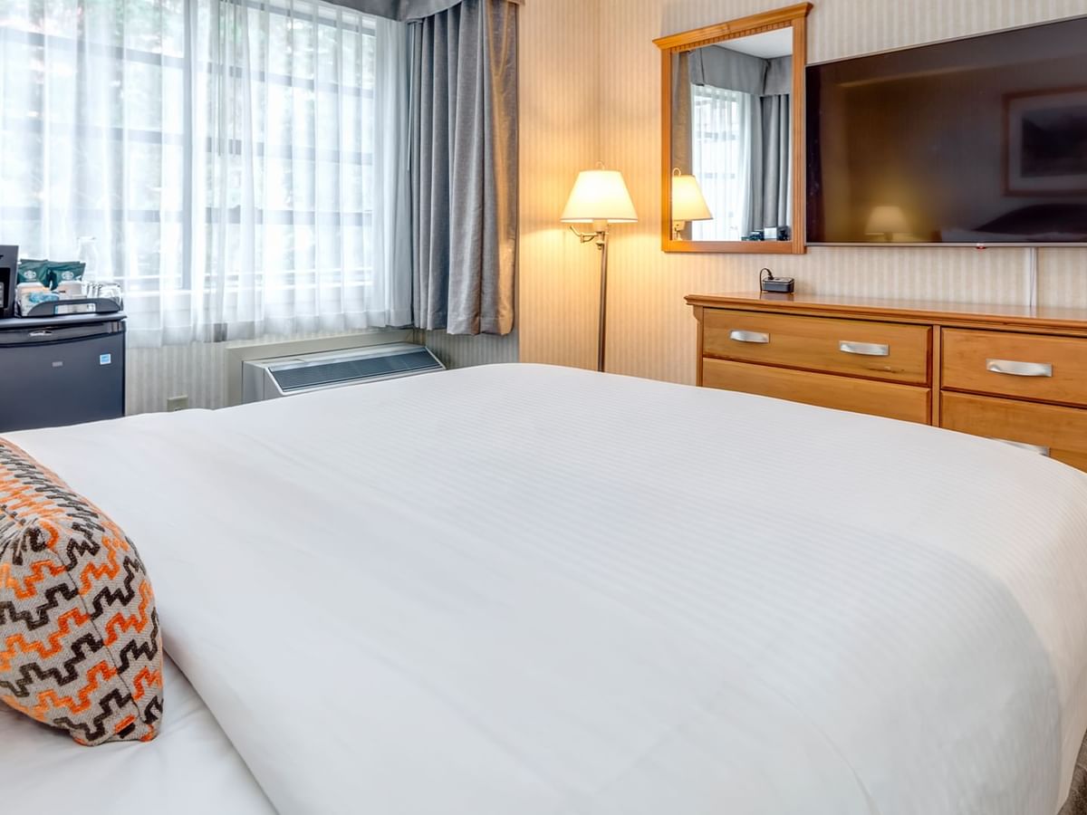 A bedroom with a large bed, TV, dresser, mirror, and a small refrigerator.