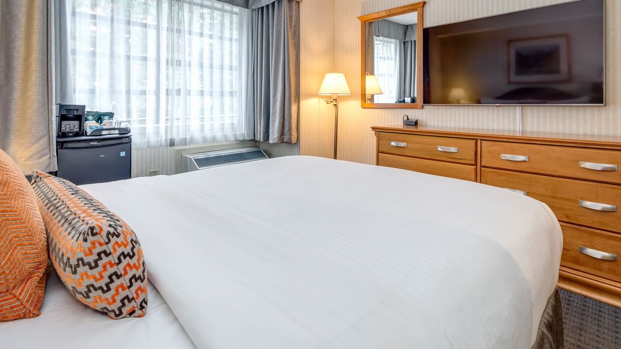 A bedroom with a large bed, TV, dresser, mirror, and a small refrigerator.