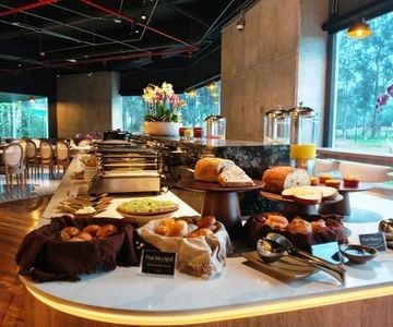 Breakfast buffet with breads and pastries on tiered stands by juice dispensers at Unika Hotels, an elite Bogota hotel