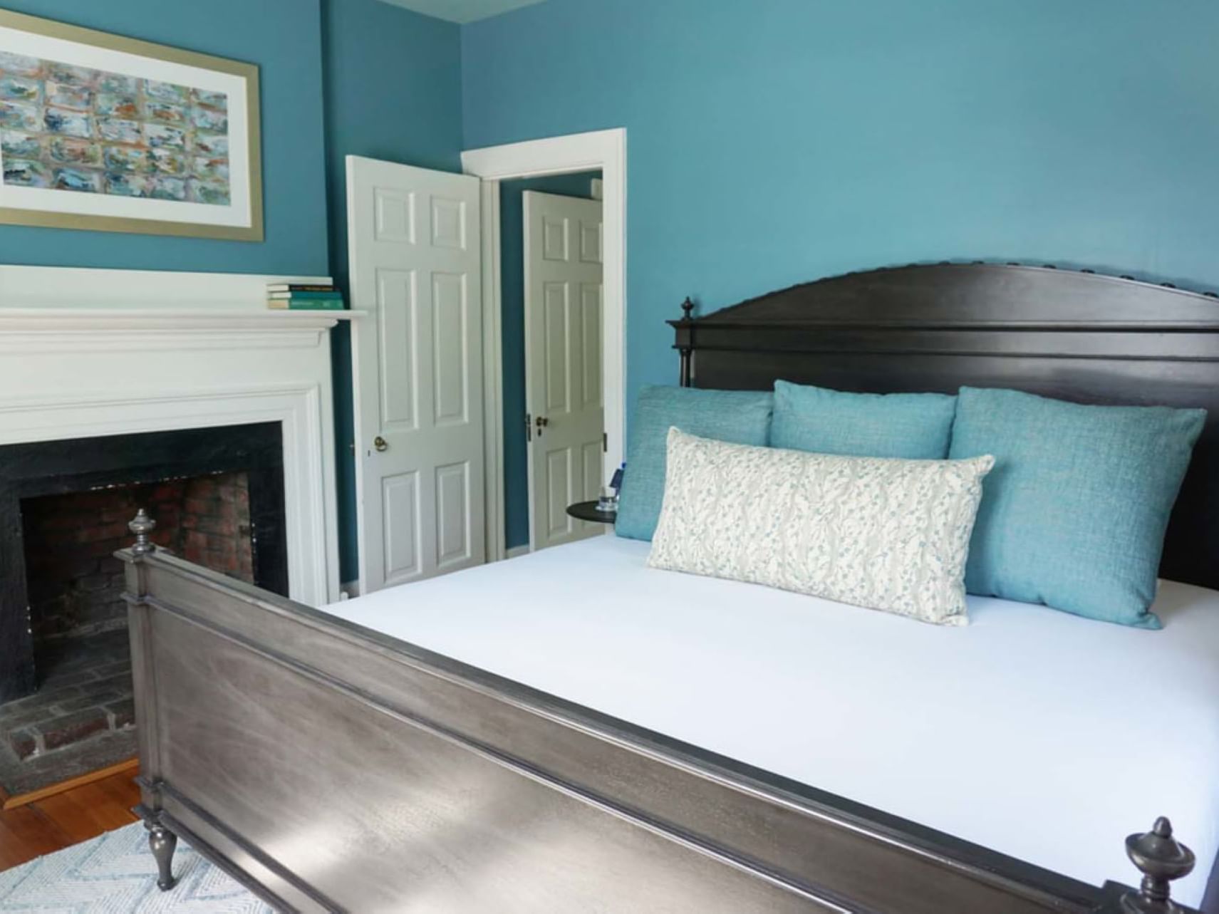 King bed with blue pillows, fireplace & wall art in Rivanna Suite at The Clifton