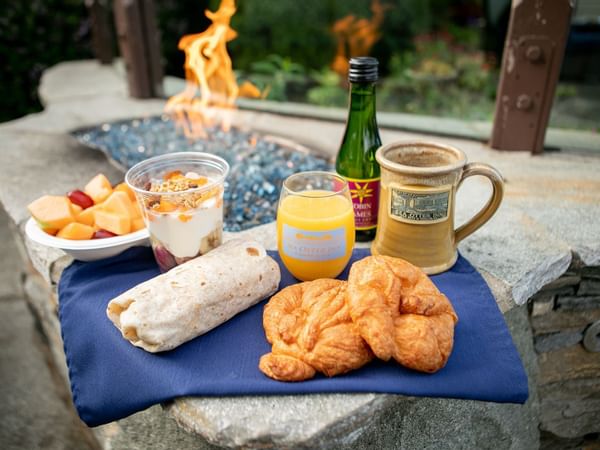 Breakfast on a blue napkin with fruit salad, orange juice, croissants, burrito, and a bottle of wine.