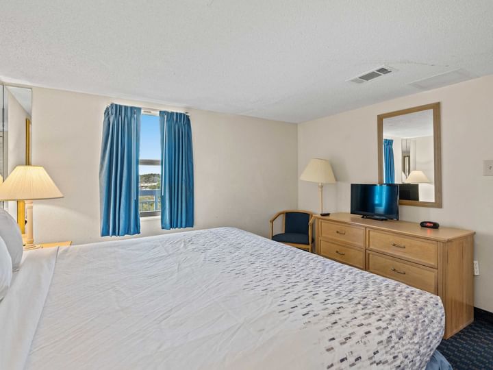 A wide-angle view of a hotel room with a large bed, dresser, and window.